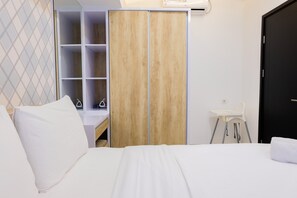 A hotel room with a bed, a wardrobe, a desk with a chair, and a white wall with a geometric pattern. - Nice and Prime Location 1BR Casa De Parco Apartment (Pagedangan)