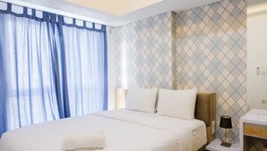 A hotel room with a large bed, a bedside table with a lamp, and a wall with a geometric pattern. - Nice and Prime Location 1BR Casa De Parco Apartment (Pagedangan)