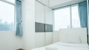 Une chambre d’hôtel moderne dotée d’un grand lit, d’une armoire avec un miroir et offrant une vue sur la ville par les fenêtres.