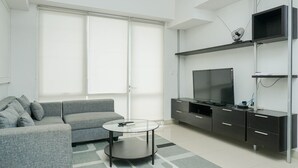 Un salon moderne avec un canapé gris, une table basse en verre et un téléviseur à écran plat posé sur un meuble.