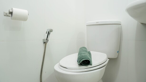 Des toilettes avec une serviette verte posée sur le siège, un porte-rouleau de papier toilette et un tuyau de douche.