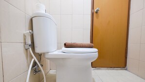 Eine weiße Toilette mit einem braunen Handtuch auf dem Sitz, einem weißen Toilettenpapierhalter und einer Holztür in einem gefliesten Badezimmer.