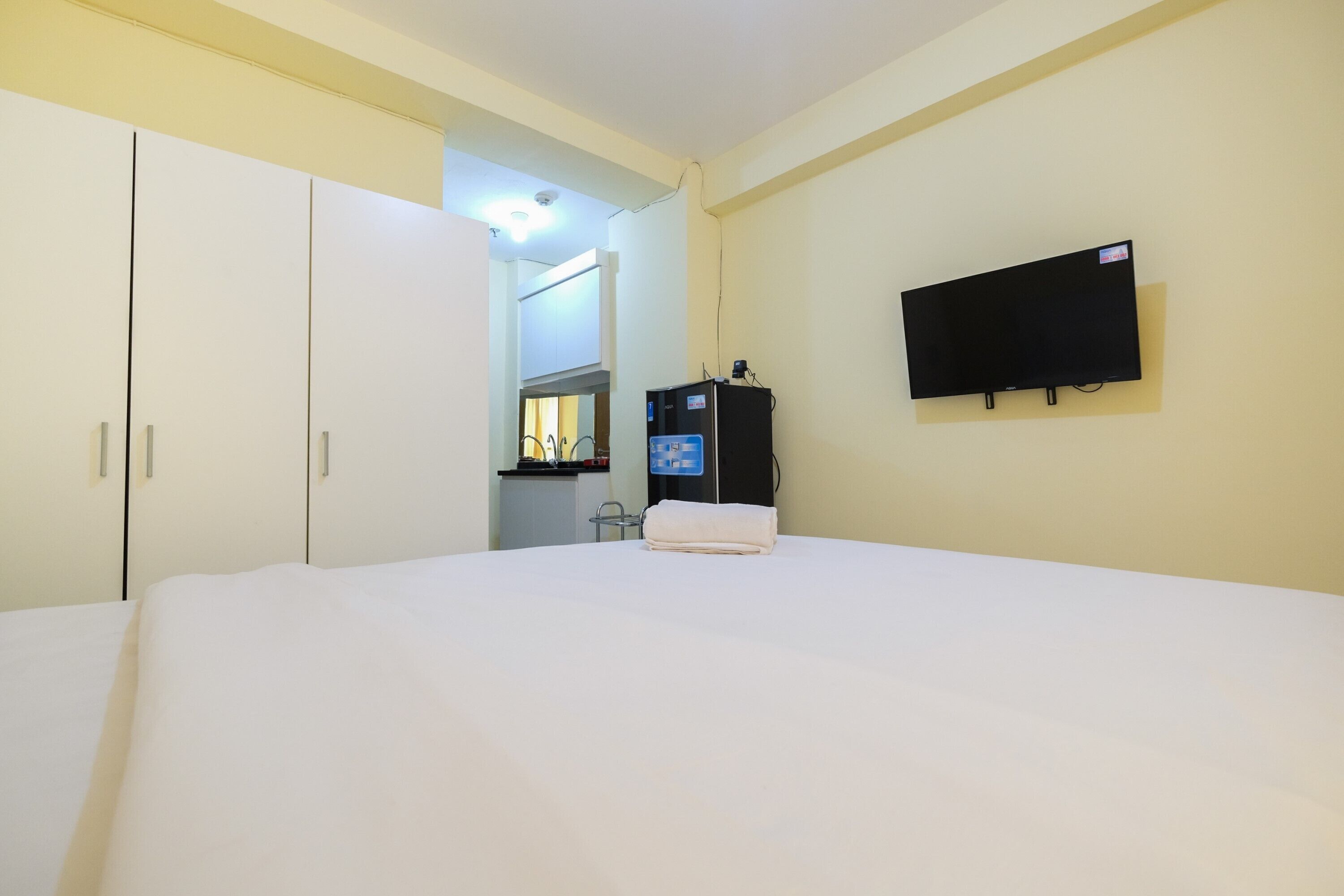 A hotel room with a bed, a TV mounted on the wall, a minibar, and a wardrobe.