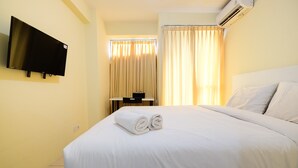 Ein Hotelzimmer mit einem Bett, einem flachbildfernseher an der Wand, einem Schreibtisch mit Stuhl und einem Fenster mit Vorhängen.
