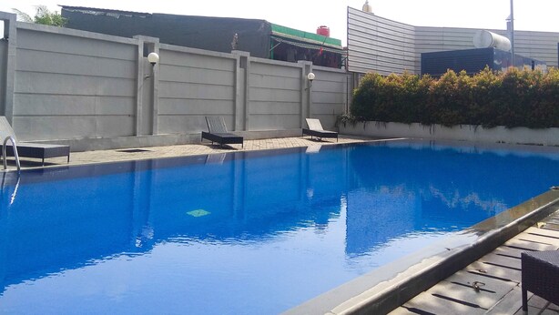 Ein Schwimmbecken mit Betonumrandung, zwei Liegestühlen und einer niedrigen Mauer mit kleinen Gartenpflanzen.