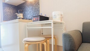 Una kitchenette con hervidor, cafetera y una caja etiquetada 'travelio'. Hay dos taburetes y un sofá gris.