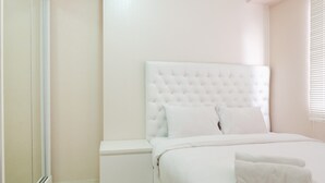 Un dormitorio con una cama blanca, una mesita de noche y una cabina de ducha de vidrio.