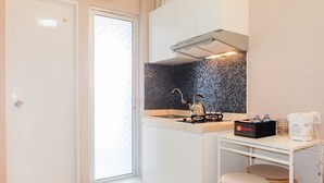Una cocina compacta con estufa a gas, hervidor y cafetera sobre una mesita.