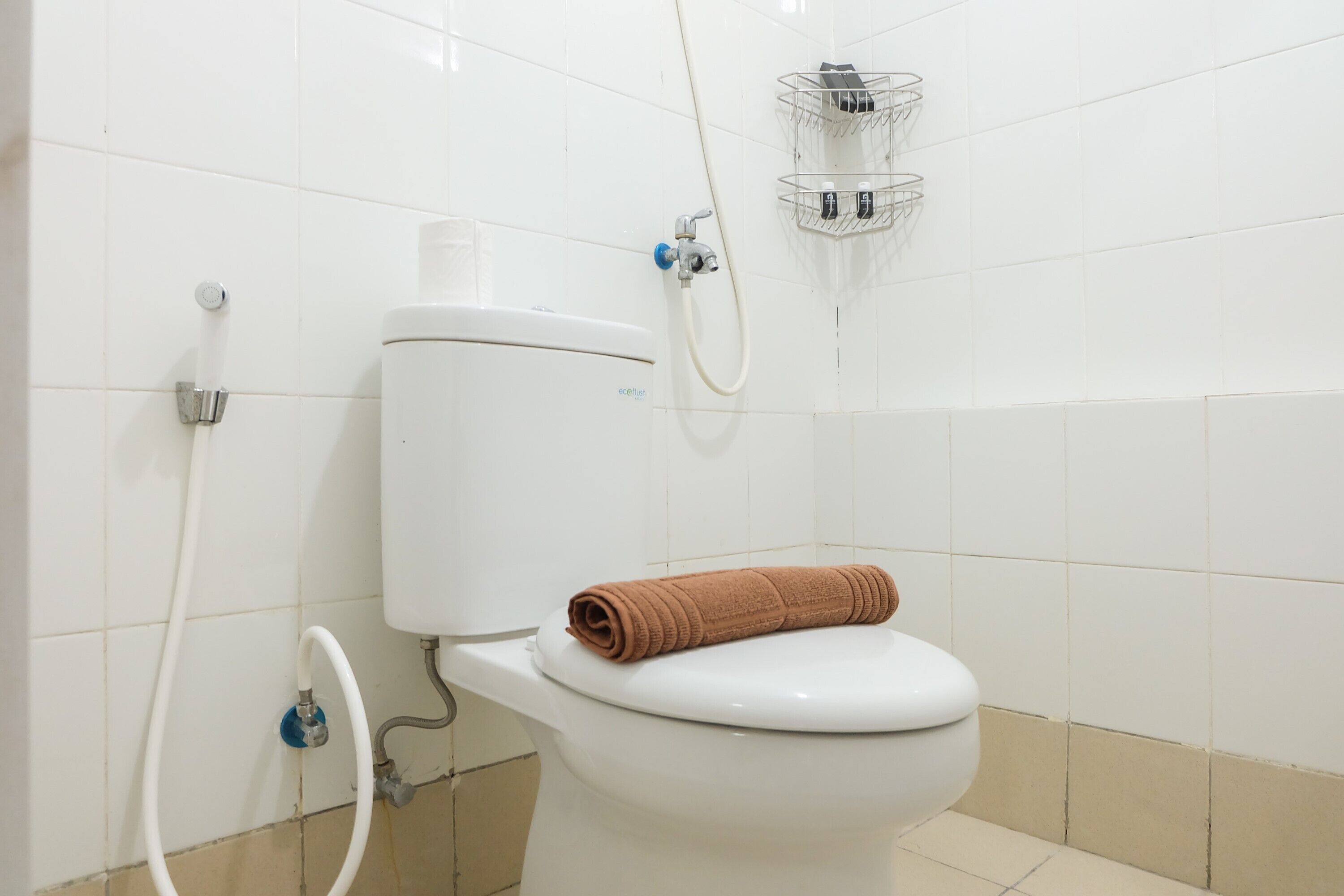 A bathroom with a white toilet, a towel on the seat, a shower head, and a toilet paper holder.