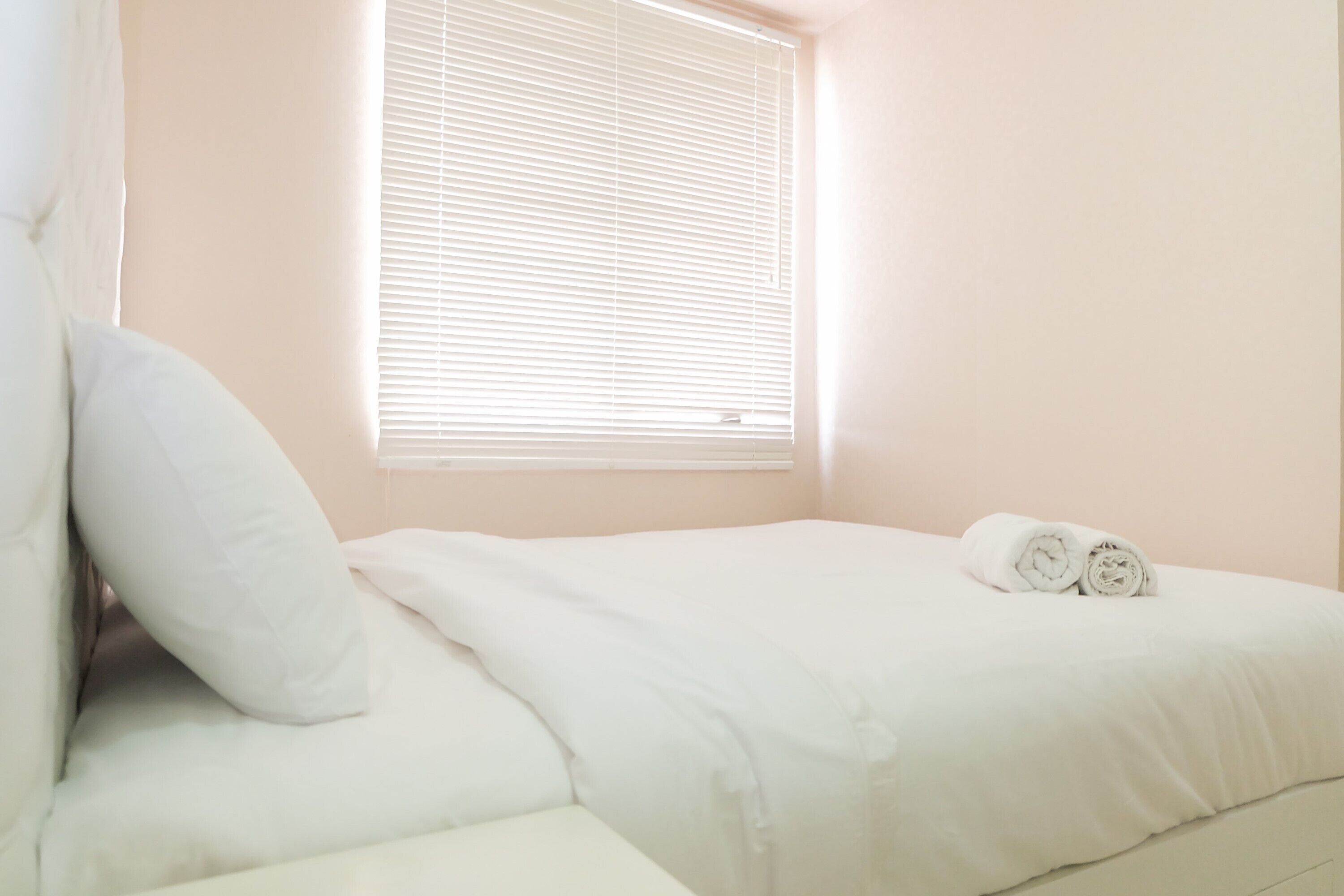 A bedroom with a bed, pillows, and a window with blinds.