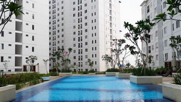 A swimming pool surrounded by planters and greenery, with high-rise buildings in the background.