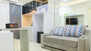A modern living area with a sofa, a small table, a TV, and a kitchenette.