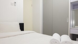 A hotel room with a neatly made bed, a bathroom with a mirror, and a door leading to another room.
