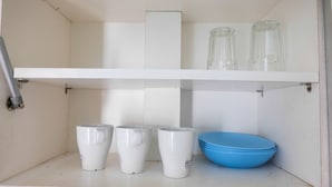 Una estantería con tazas blancas, un bol azul y dos vasos de vidrio.