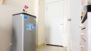 Un refrigerador compacto y moderno con una etiqueta que indica que es de la habitación del séptimo piso, ubicado en un pasillo con una puerta blanca y piso de baldosas.