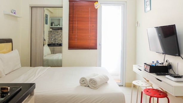 Habitación de hotel con cama, escritorio con televisor, taburete pequeño y baño visible a través de una puerta abierta.