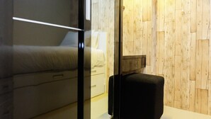 A bedroom with a bed, bedside table, and a small black ottoman.