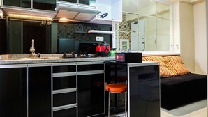 A modern kitchen with a built-in stove, a coffee machine, and a small refrigerator. There is a black countertop and a black bar stool.