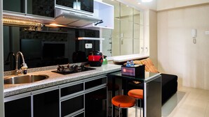 A modern kitchen with a stainless steel sink, a built-in stove, and a range hood. There are two bar stools and a small table with a box labeled "TraVello".