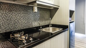 A modern kitchen with a black countertop, stainless steel sink, and a tiled backsplash. - Brand New Studio Room at Bintaro Icon Apartment (South Tangerang)
