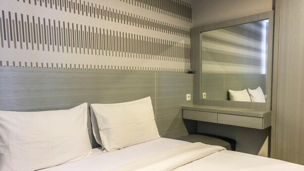 A hotel room with a bed, a bedside table, a mirror, and a wall with a vertical striped pattern. - Brand New Studio Room at Bintaro Icon Apartment (South Tangerang)