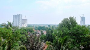 A high-rise building with construction cranes, surrounded by dense greenery and palm trees. - Brand New Studio Room at Bintaro Icon Apartment (South Tangerang)