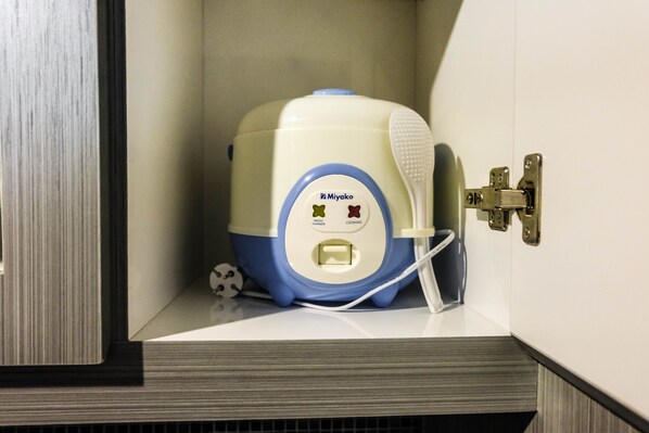 A compact kitchen appliance with a control panel, a power cord, and a white brush attachment.