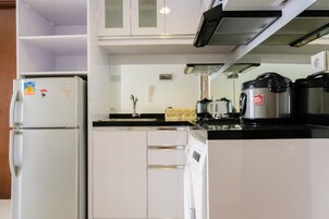 Una cocina compacta con gabinetes blancos, horno integrado, cafetera y microondas.