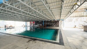 Una piscina techada con piso de baldosas y estructura de techo metálica.