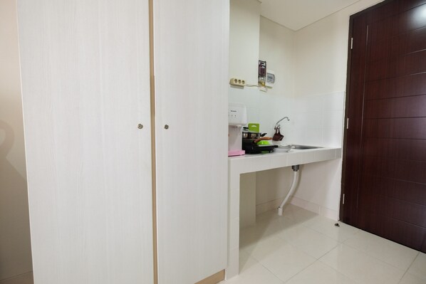A small kitchen with a white countertop, a sink, and a dark wooden door.