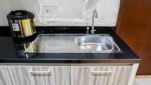A kitchen with a stainless steel sink, a black countertop, and a microwave. - Premium 1BR Apartement At Grand Sungkono Lagoon (Surabaya)