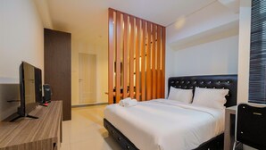 A hotel room with a bed, a desk with a television, and a wooden partition. - Elegant 1BR at Grand Kamala Lagoon Apartment (Bekasi)