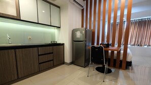 A modern kitchen with a refrigerator, a sink, and a dining area with a chair and table. - Elegant 1BR at Grand Kamala Lagoon Apartment (Bekasi)
