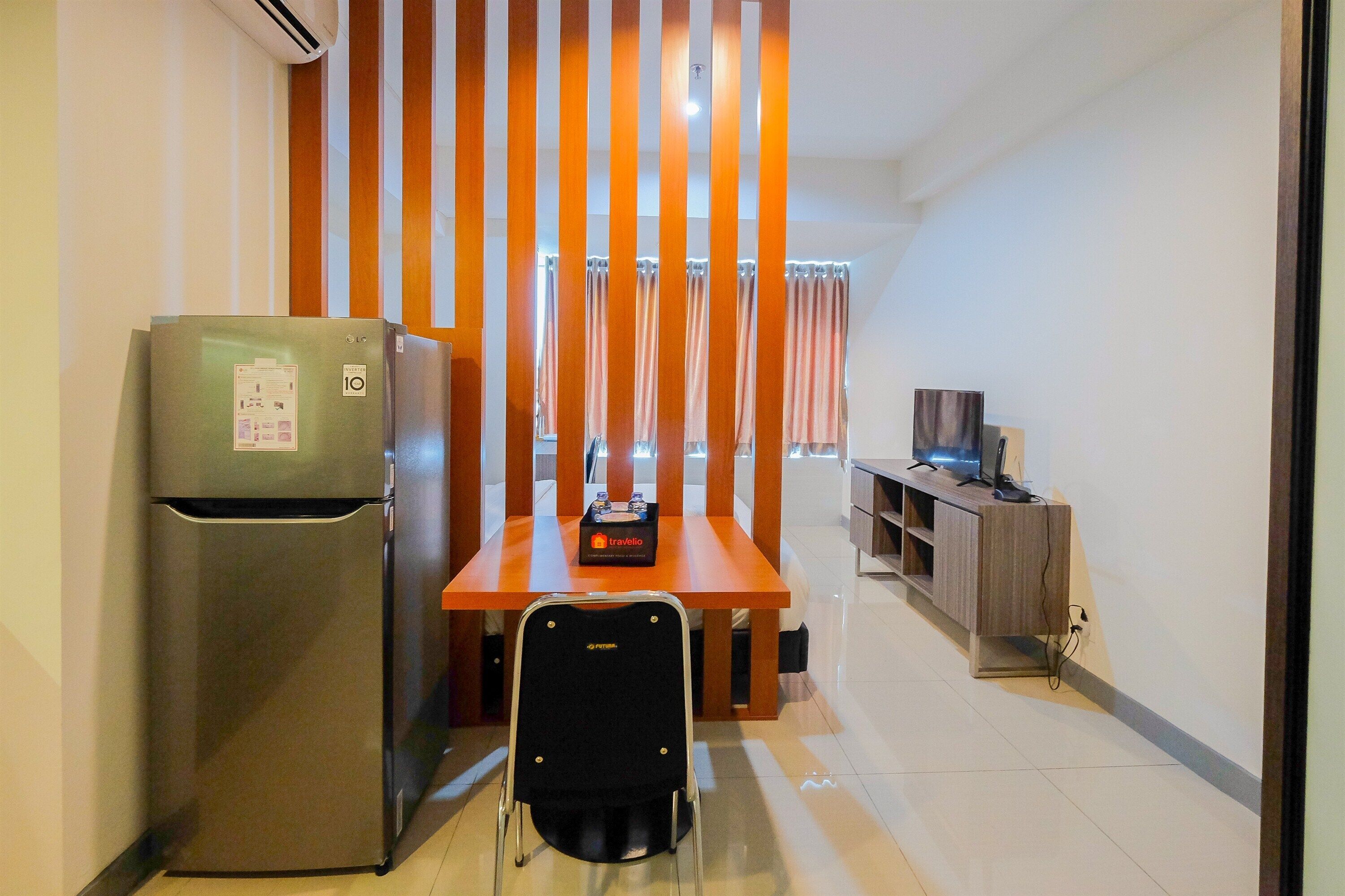 A compact hotel room with a kitchenette, a dining table, a chair, a TV, and a curtain divider.