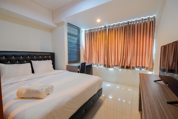 A hotel room with a large bed, a desk, and a window with curtains. - Elegant 1BR at Grand Kamala Lagoon Apartment (Bekasi)