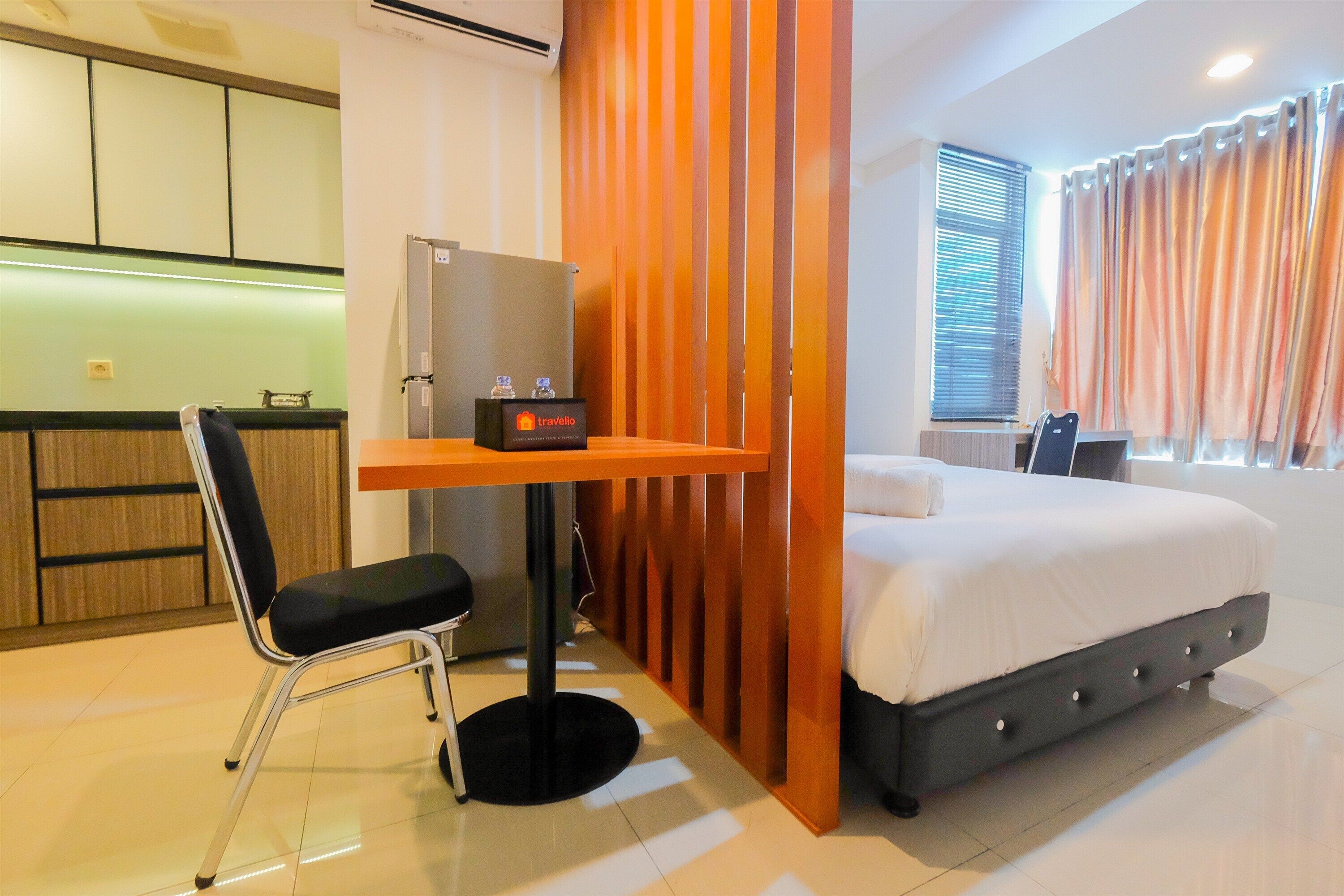 A hotel room with a bed, a desk with a chair, a minibar, and a view of the outside through a window with curtains.