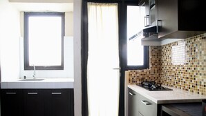 A kitchen with dark cabinets, a window, a tiled backsplash, and a stove. - Best Deal Studio at Kebagusan City Apartment (Jakarta)