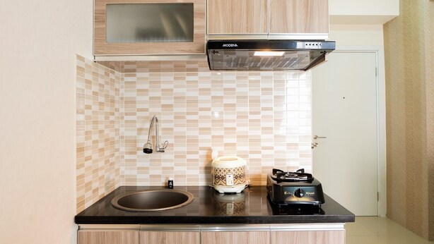 A kitchen with a black countertop, a sink, a microwave, a stove, and a patterned backsplash. - Comfortable Fully Furnished Studio Green Pramuka City Apartment (Jakarta)