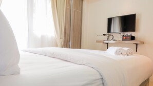 A hotel room with a bed, a TV mounted on the wall, and a minibar. - Comfortable Fully Furnished Studio Green Pramuka City Apartment (Jakarta)