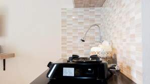 A kitchen with a modern stove, a sink, and a tiled backsplash. - Comfortable Fully Furnished Studio Green Pramuka City Apartment (Jakarta)