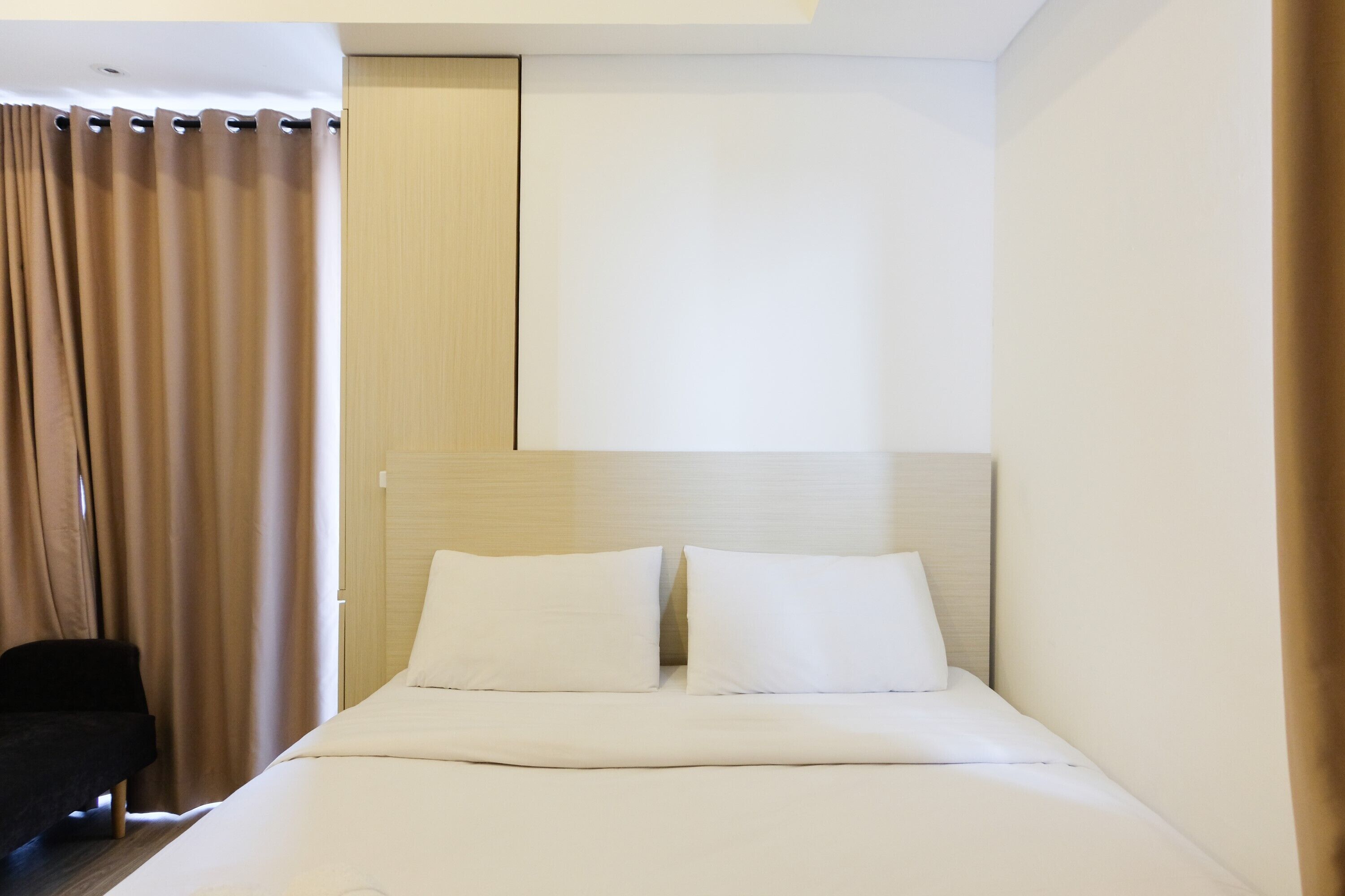 A neatly made bed with white linens, a headboard, and a black chair in a hotel room.