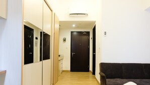 Een hotelkamer met een bed, een donkerbruine bank, een houten garderobe en een deur met een codeerapparaat.
