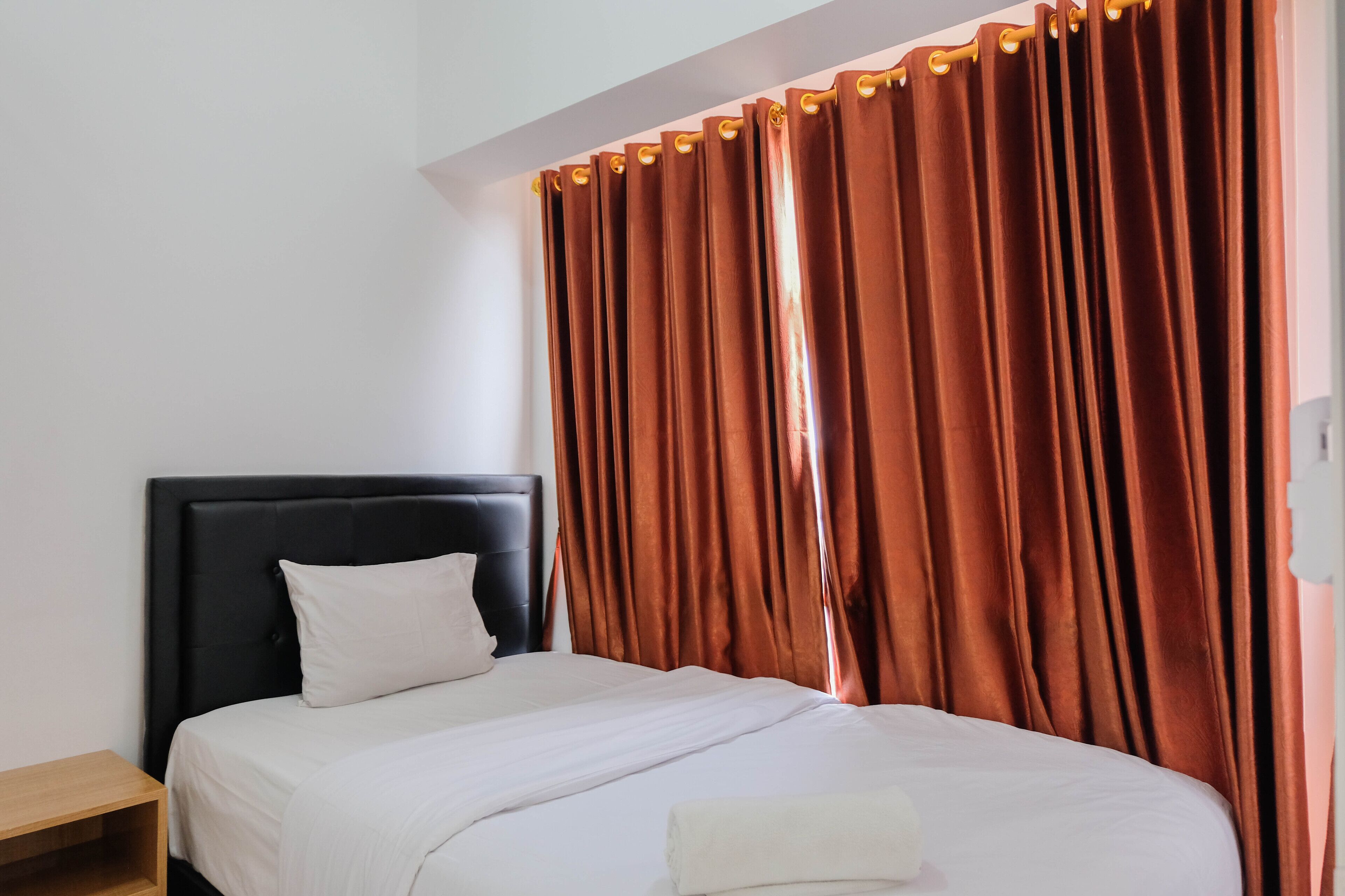 A neatly made bed with white linens, a black headboard, and a wooden nightstand.