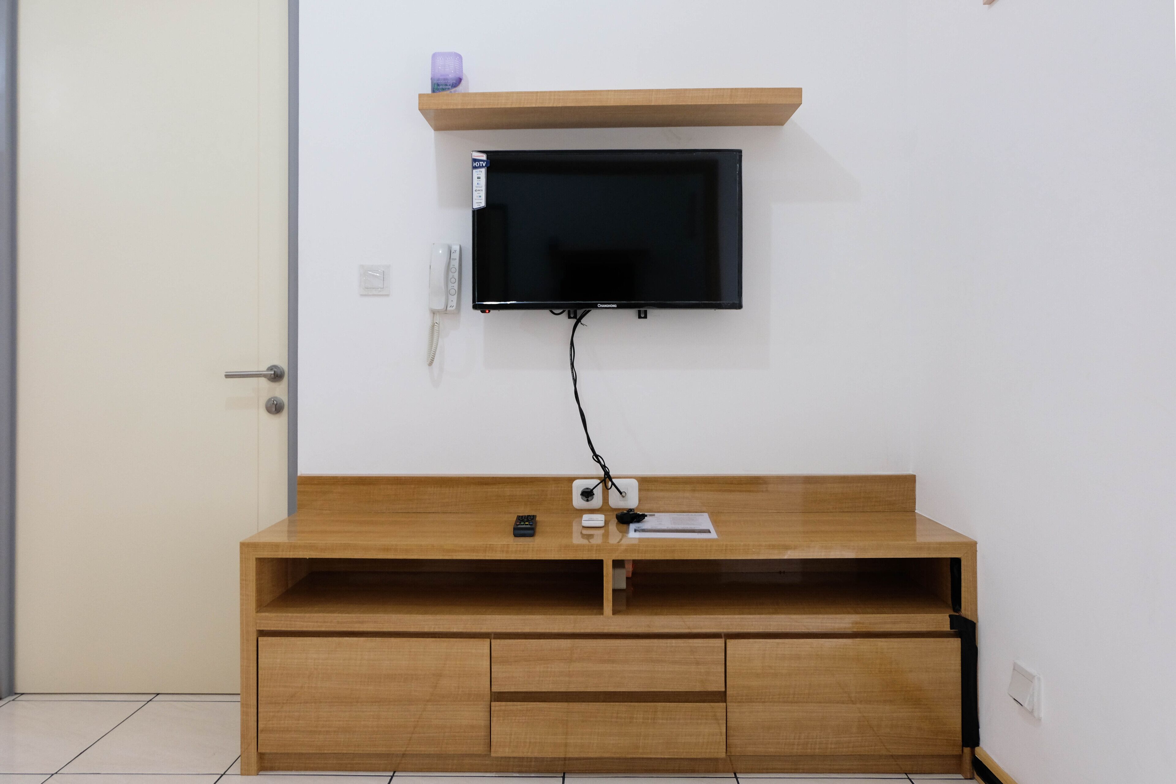 A room with a wooden TV stand, a mounted TV, and a door.