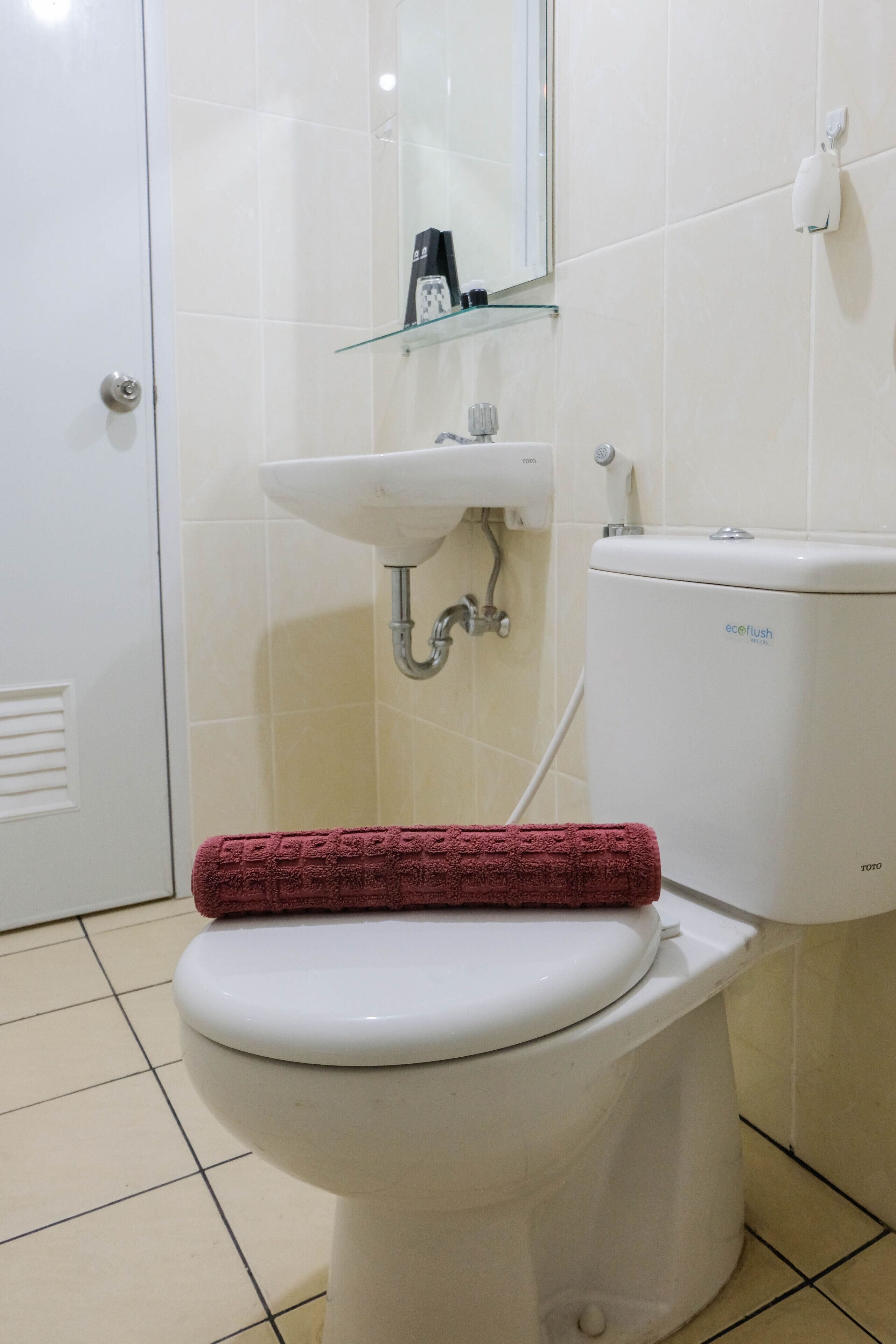 Un baño con un inodoro blanco, un estante de vidrio sobre el lavabo y un espejo en la pared.