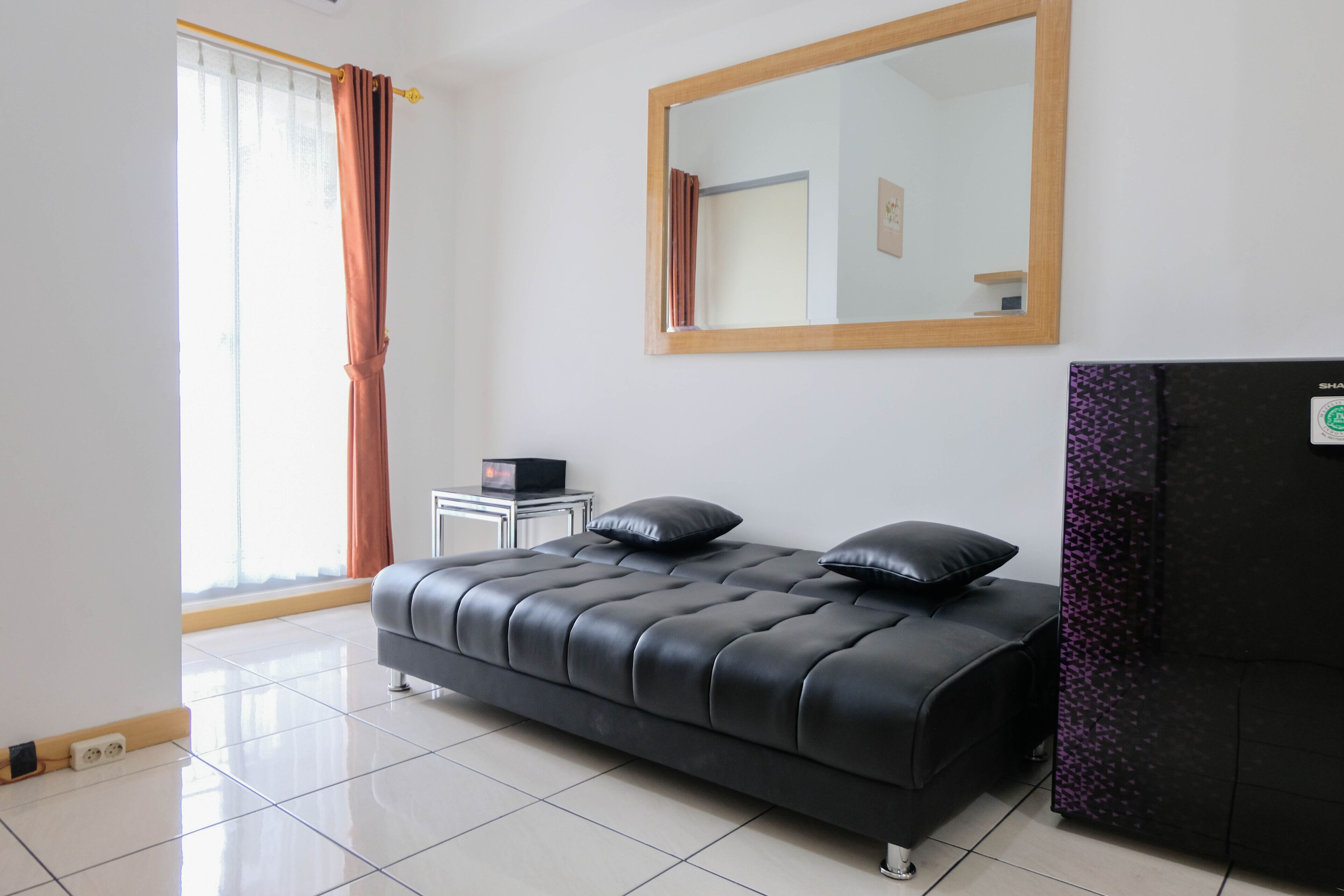 Un dormitorio moderno con un sofá de cuero negro, un espejo grande y una mesita de noche.