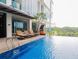 A modern hotel with a rooftop infinity pool, lounge chairs, and a view of lush greenery.