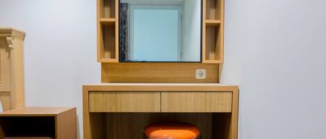 A room with a wooden desk, a stool, a mirror, and an air conditioning unit.