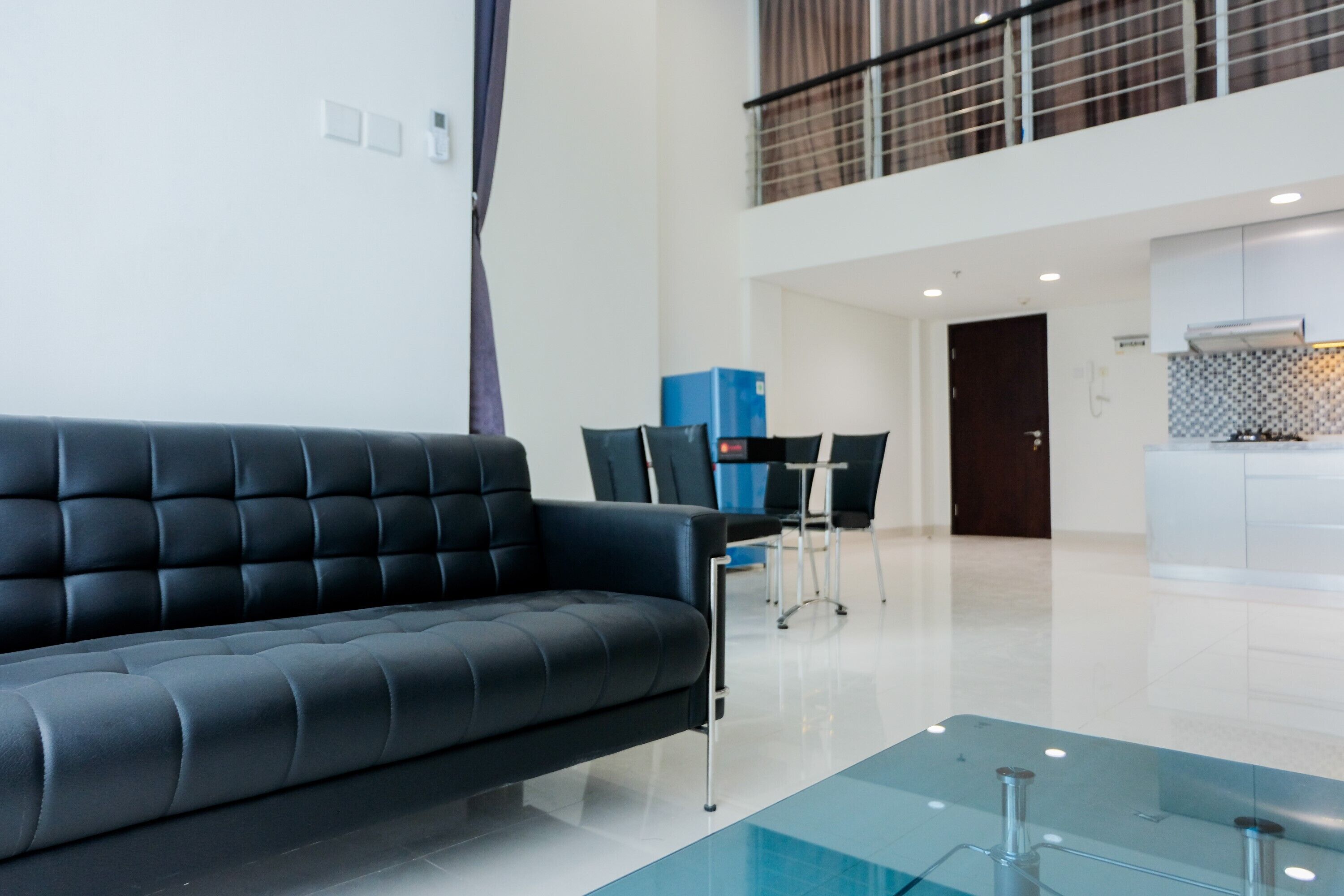 A modern living room with a black sofa, a glass coffee table, and a dining area with chairs and a table.