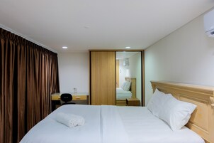 A hotel room with a neatly made bed, a desk with a chair, a wardrobe, and a mirror.